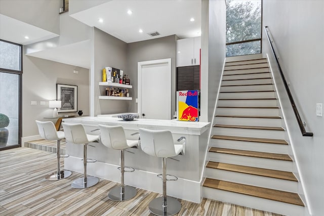 bar featuring recessed lighting, bar, visible vents, stairs, and light wood finished floors