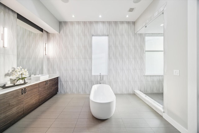 full bathroom featuring tile walls, visible vents, a freestanding bath, vanity, and tile patterned floors