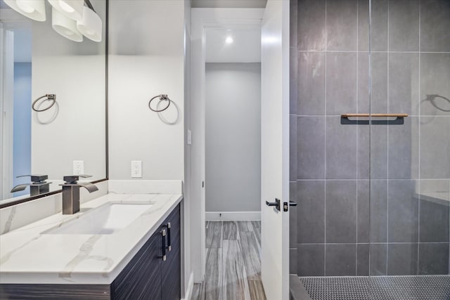 full bathroom with wood finished floors, a tile shower, vanity, and baseboards