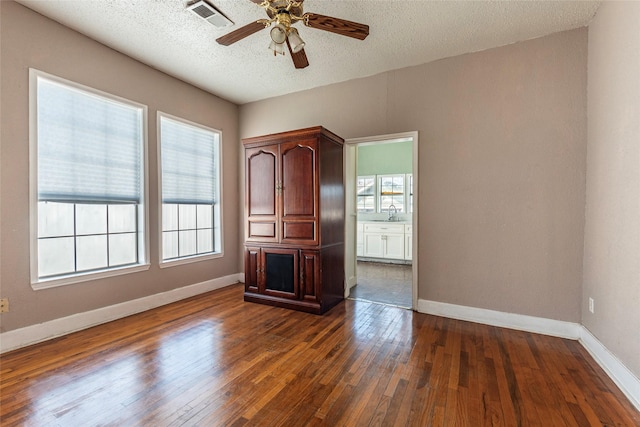 spare room featuring a textured ceiling, a wealth of natural light, dark wood finished floors, and visible vents