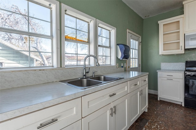 kitchen with light countertops, white microwave, white cabinets, a sink, and black / electric stove