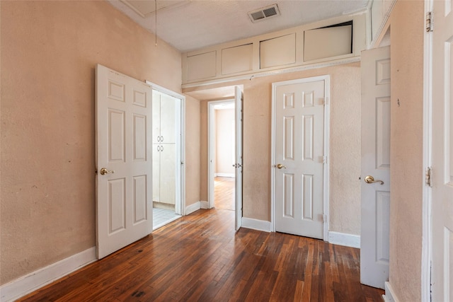 unfurnished bedroom featuring dark wood-style floors, attic access, visible vents, and baseboards