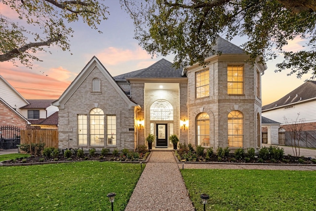 french country style house with brick siding, a shingled roof, a yard, and fence