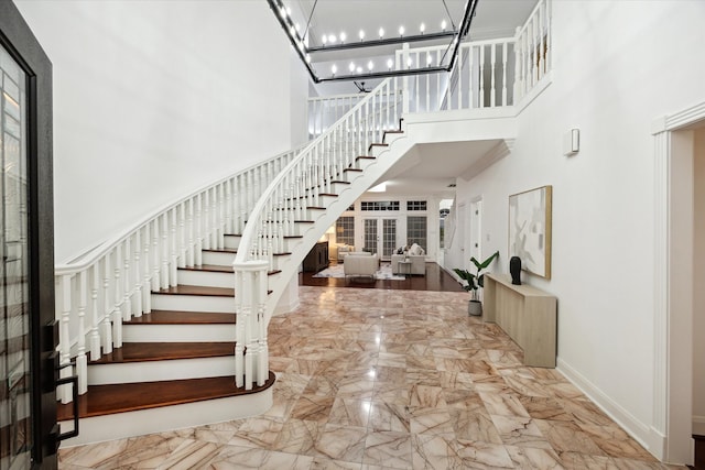 foyer entrance featuring stairway, baseboards, a towering ceiling, a notable chandelier, and marble finish floor