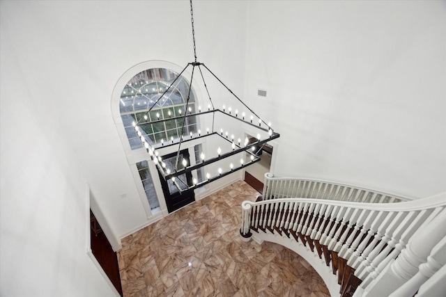 stairway with visible vents, marble finish floor, an inviting chandelier, baseboards, and a towering ceiling