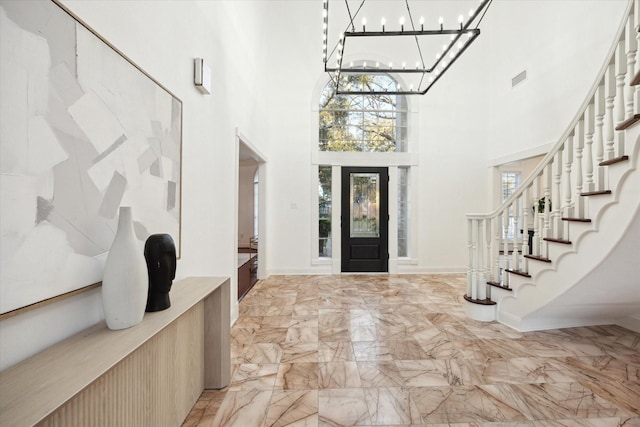 foyer with a chandelier, marble finish floor, baseboards, and a towering ceiling