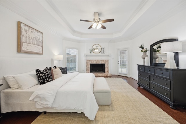 bedroom with dark wood-style floors, a premium fireplace, access to exterior, crown molding, and a raised ceiling