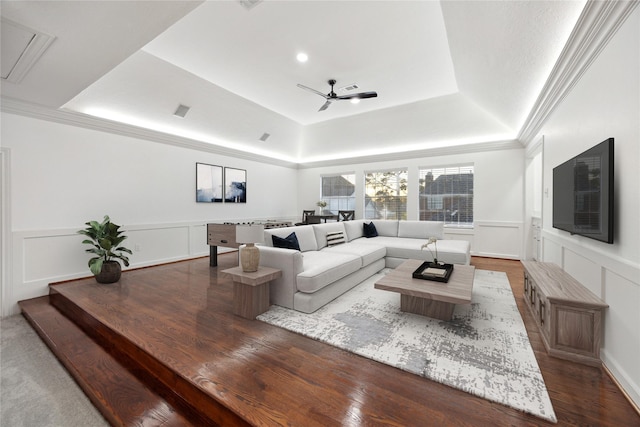 living room with crown molding, ceiling fan, a wainscoted wall, a decorative wall, and a raised ceiling