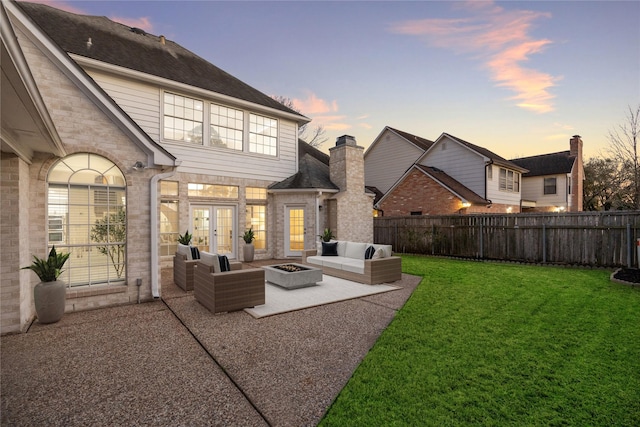 back of property at dusk featuring a patio, a fenced backyard, french doors, stone siding, and a lawn