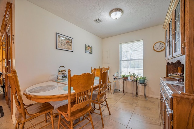 dining room featuring light tile patterned floors, visible vents, baseboards, and a textured ceiling