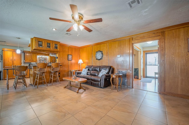 living room with light tile patterned floors, visible vents, wood walls, and a textured ceiling