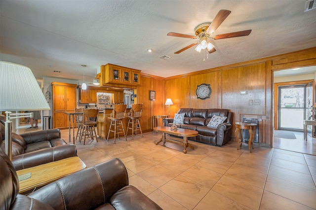 living room featuring light tile patterned flooring, visible vents, wood walls, and a textured ceiling