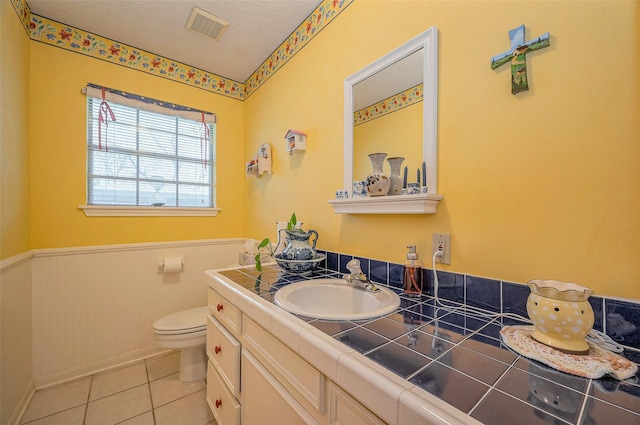 bathroom featuring vanity, a wainscoted wall, visible vents, tile patterned flooring, and toilet