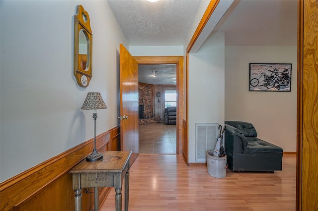 hall featuring visible vents, light wood-style flooring, and a textured ceiling