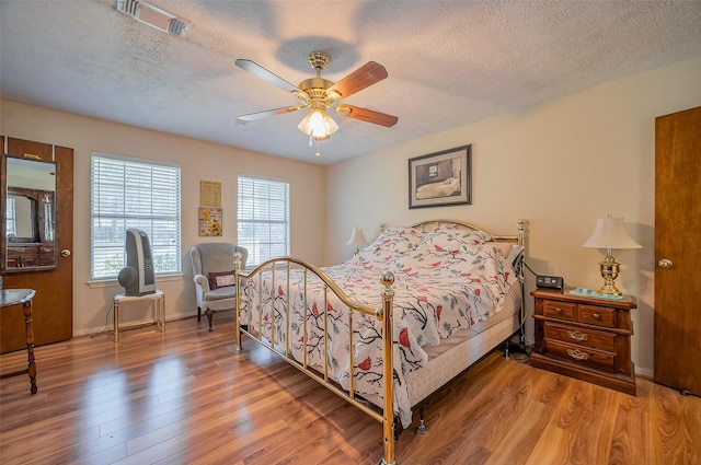 bedroom with visible vents, a textured ceiling, ceiling fan, and wood finished floors