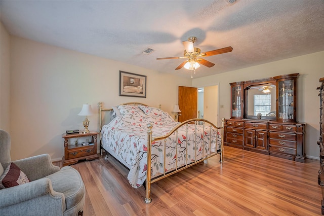 bedroom featuring visible vents, baseboards, ceiling fan, light wood-style flooring, and a textured ceiling