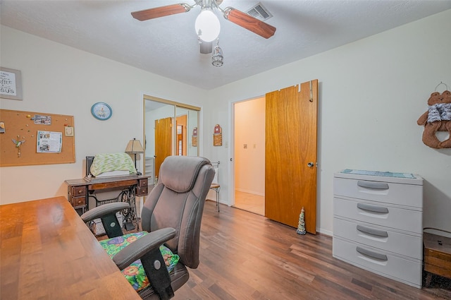 home office featuring visible vents, a textured ceiling, wood finished floors, baseboards, and ceiling fan