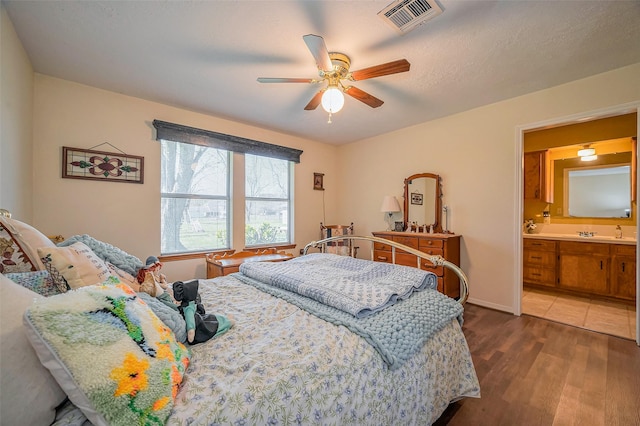 bedroom with a ceiling fan, wood finished floors, visible vents, baseboards, and ensuite bathroom