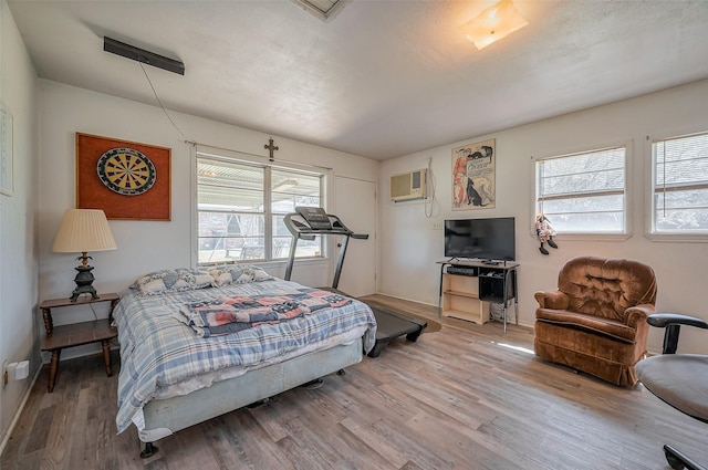 bedroom with multiple windows, an AC wall unit, and wood finished floors