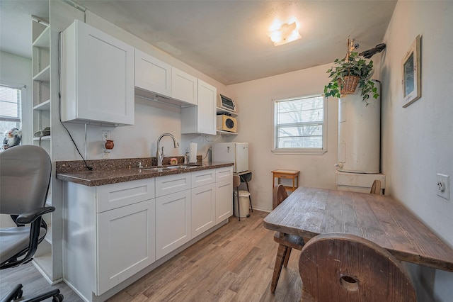 kitchen with a sink, light wood finished floors, a wealth of natural light, and white cabinetry