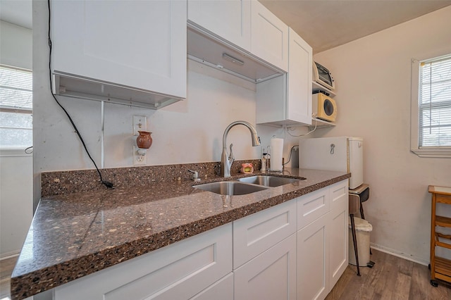 kitchen with baseboards, dark stone countertops, wood finished floors, white cabinets, and a sink