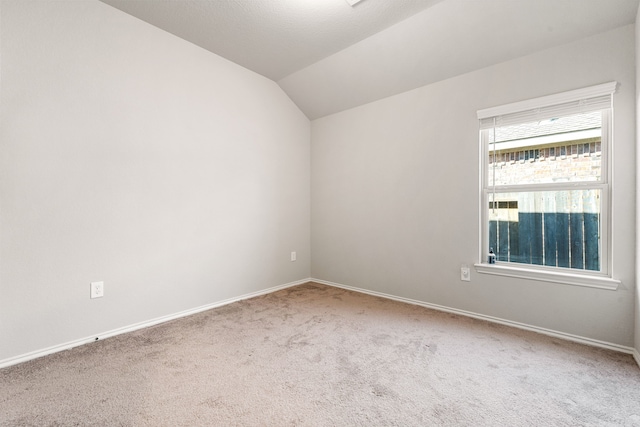 spare room featuring lofted ceiling, carpet flooring, and baseboards