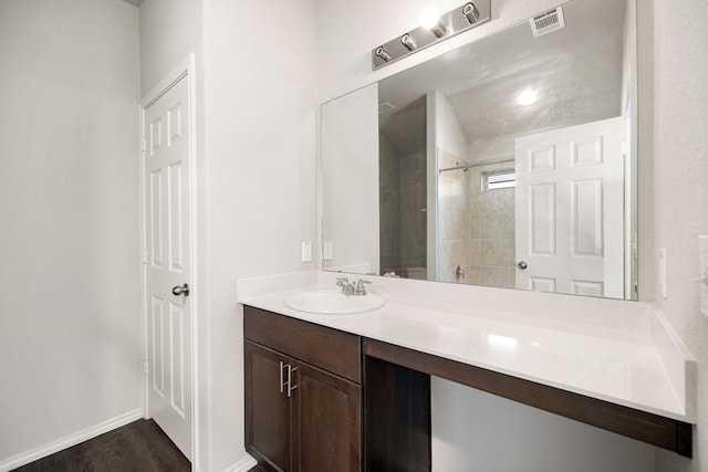 bathroom featuring visible vents, vanity, wood finished floors, baseboards, and walk in shower