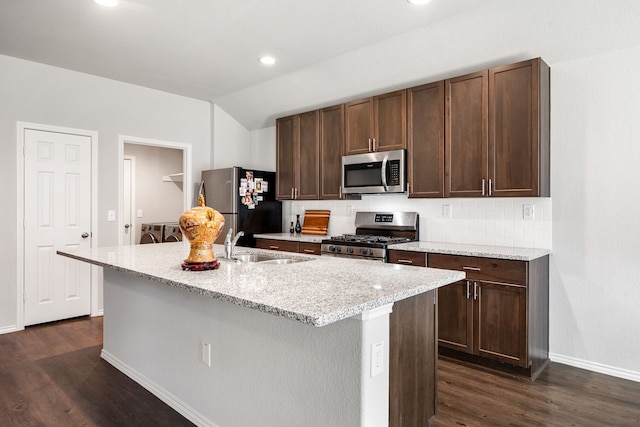 kitchen with lofted ceiling, a kitchen island with sink, a sink, appliances with stainless steel finishes, and dark wood-style floors