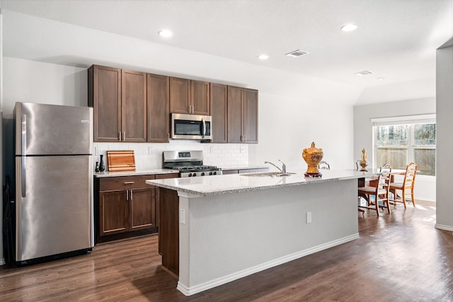 kitchen with appliances with stainless steel finishes, dark wood-type flooring, a sink, and backsplash