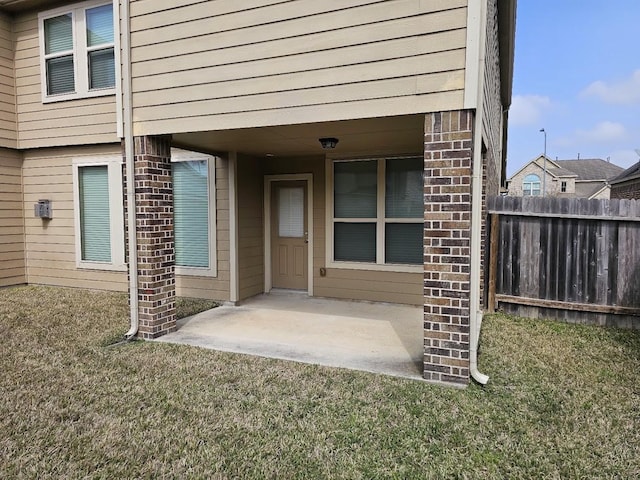 view of exterior entry with a yard, fence, and brick siding