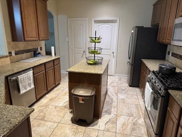 kitchen with light stone counters, backsplash, a kitchen island, stainless steel appliances, and baseboards