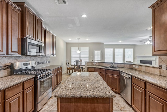 kitchen with visible vents, light stone countertops, a center island, decorative backsplash, and appliances with stainless steel finishes