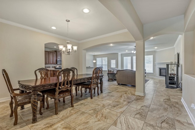 dining space featuring arched walkways, crown molding, a glass covered fireplace, and ceiling fan with notable chandelier