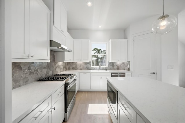 kitchen with decorative backsplash, appliances with stainless steel finishes, white cabinetry, a sink, and wall chimney exhaust hood