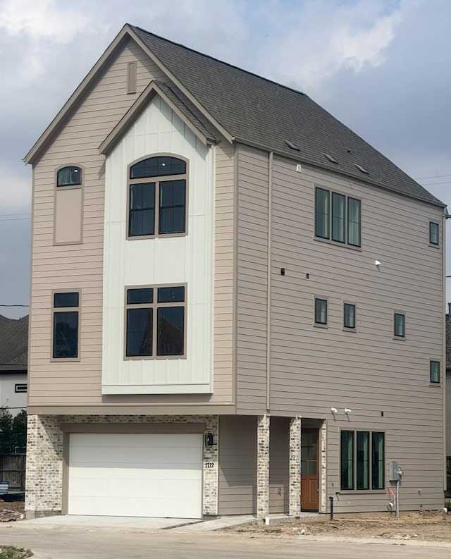 exterior space with driveway, an attached garage, board and batten siding, and roof with shingles