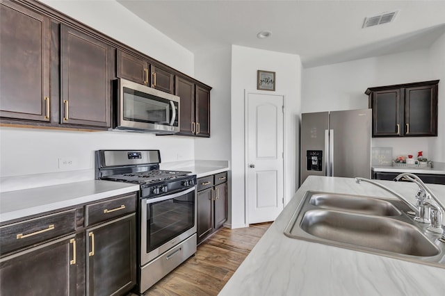 kitchen featuring visible vents, a sink, stainless steel appliances, light countertops, and dark wood-type flooring