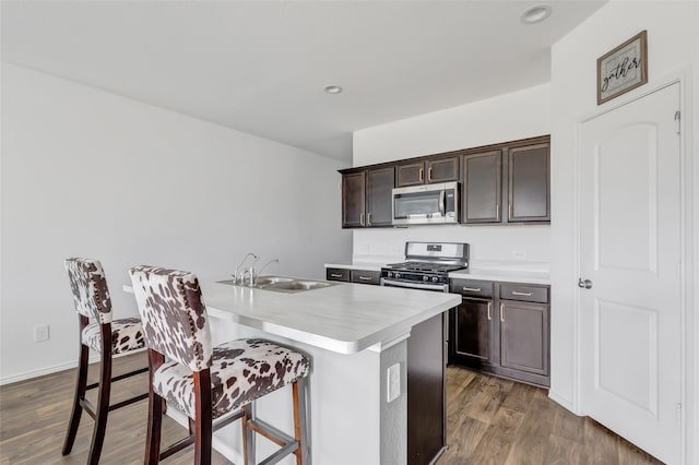 kitchen with a breakfast bar area, a sink, stainless steel appliances, dark brown cabinetry, and light countertops