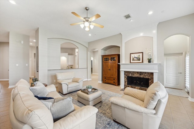 living room featuring a high end fireplace, light tile patterned floors, recessed lighting, arched walkways, and a ceiling fan