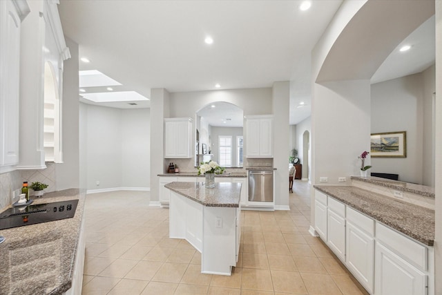 kitchen featuring backsplash, light tile patterned flooring, arched walkways, white cabinets, and stainless steel dishwasher