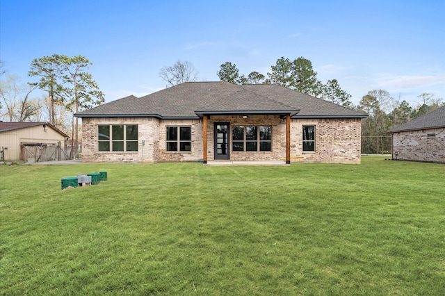 back of property featuring brick siding, roof with shingles, and a yard