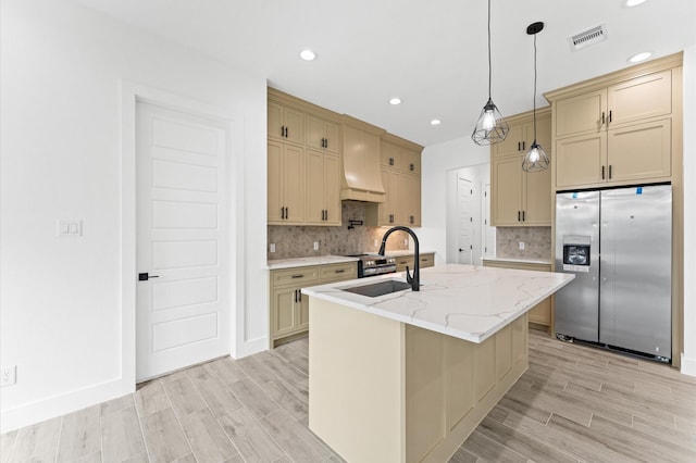 kitchen with a sink, stainless steel fridge with ice dispenser, custom exhaust hood, wood tiled floor, and an island with sink