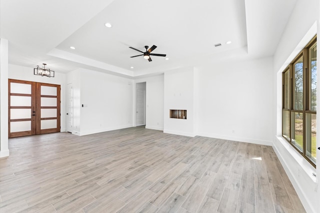 unfurnished living room with french doors, light wood finished floors, and a raised ceiling