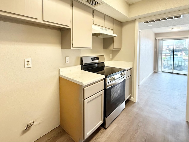 kitchen featuring under cabinet range hood, visible vents, baseboards, electric stove, and light wood-type flooring