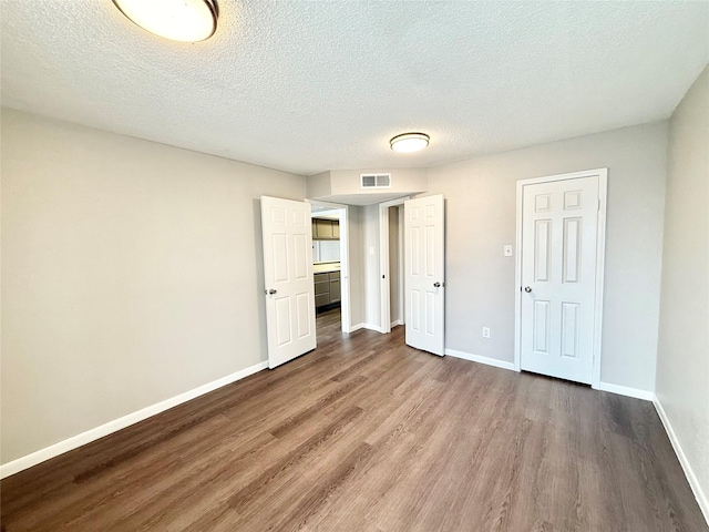 unfurnished bedroom with a textured ceiling, wood finished floors, visible vents, and baseboards