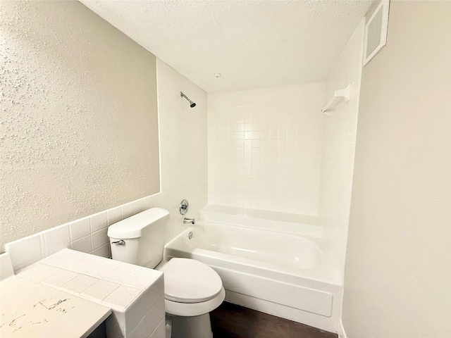 bathroom with a textured ceiling, a textured wall, toilet, bathing tub / shower combination, and visible vents