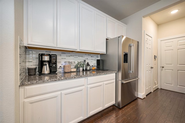 kitchen featuring dark stone counters, white cabinets, stainless steel fridge with ice dispenser, decorative backsplash, and dark wood-style floors