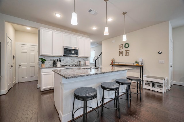 kitchen featuring dark wood-type flooring, a sink, visible vents, light stone countertops, and stainless steel microwave