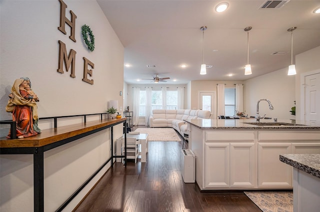 kitchen with dark wood finished floors, visible vents, white cabinets, a sink, and dark stone counters