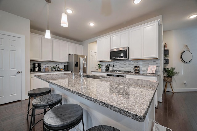 kitchen with stainless steel appliances, a breakfast bar, backsplash, a sink, and white cabinetry