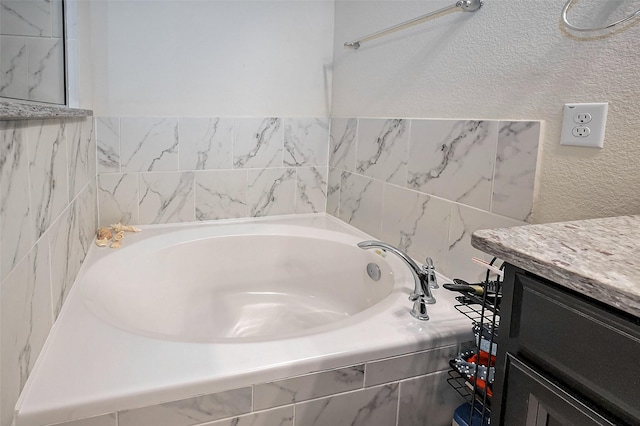 full bath with a textured wall, a garden tub, and vanity